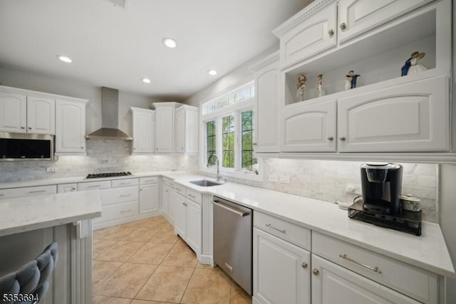 kitchen featuring decorative backsplash, wall chimney exhaust hood, white cabinets, a sink, and stainless steel appliances