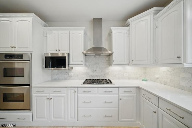 kitchen featuring decorative backsplash, white cabinets, wall chimney range hood, and stainless steel appliances