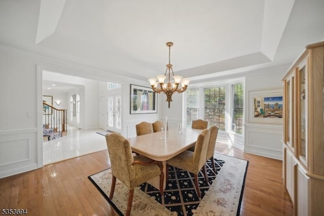 dining area featuring a decorative wall, a tray ceiling, light wood-style flooring, and a notable chandelier