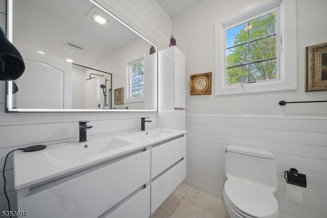 full bath with toilet, a sink, wainscoting, and a wealth of natural light