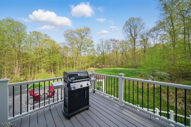 wooden terrace with a lawn, a grill, and a forest view