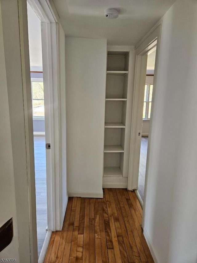hallway with baseboards, built in features, and hardwood / wood-style flooring