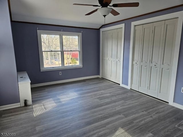 unfurnished bedroom featuring wood finished floors, baseboards, ceiling fan, and two closets