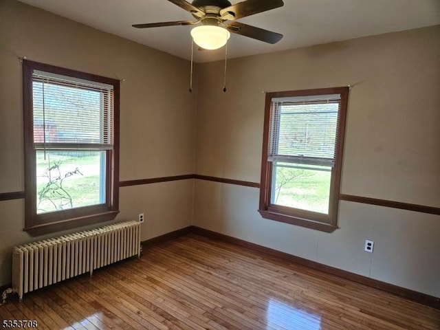 empty room with baseboards, a wealth of natural light, radiator heating unit, and light wood-style flooring