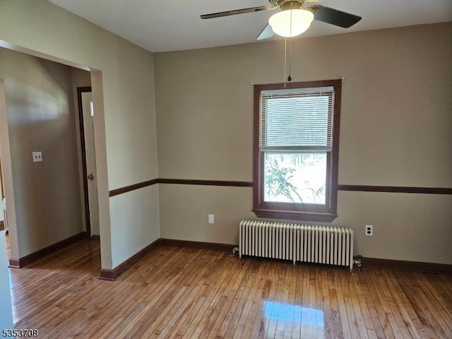 spare room featuring radiator heating unit, baseboards, ceiling fan, and wood-type flooring