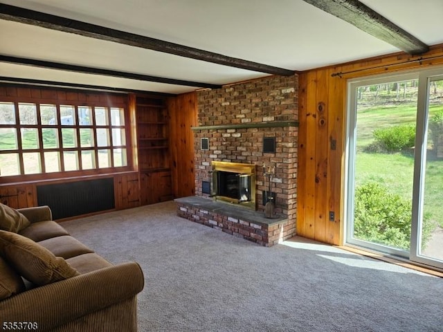 living room featuring wooden walls, carpet flooring, a brick fireplace, and beam ceiling