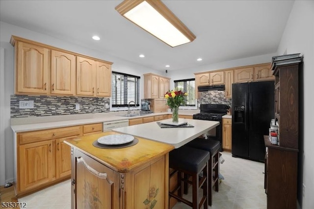 kitchen with black appliances, a center island, light brown cabinets, light countertops, and decorative backsplash