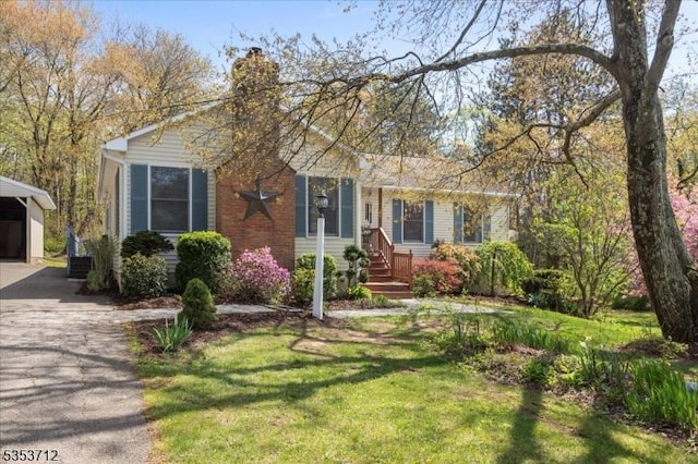 view of front of property with a front yard, a chimney, concrete driveway, and an outbuilding