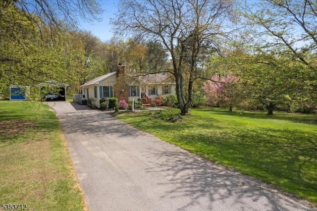 view of front of house featuring driveway, a front lawn, a chimney, and a carport