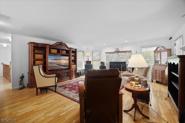 living area with healthy amount of natural light, light wood-style flooring, a stone fireplace, baseboards, and recessed lighting