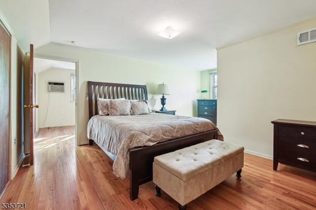 bedroom featuring an AC wall unit, baseboards, visible vents, vaulted ceiling, and wood finished floors