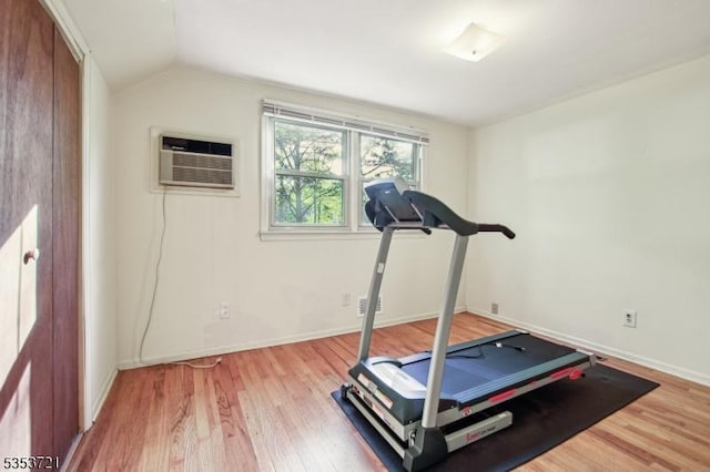 workout area with vaulted ceiling, light wood finished floors, baseboards, and a wall unit AC