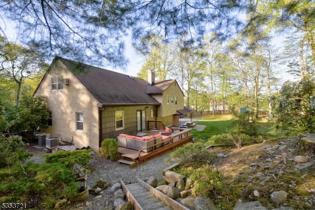 rear view of property with stucco siding, a wooden deck, a chimney, central AC unit, and a shingled roof