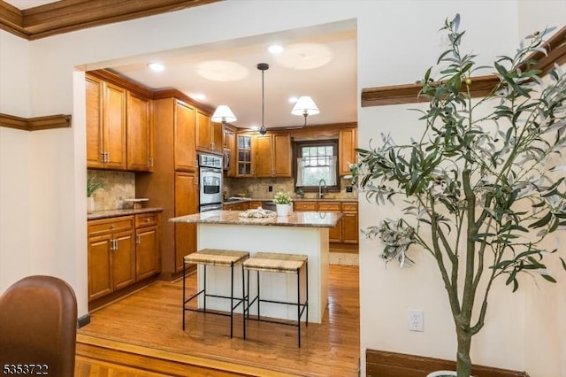 kitchen featuring brown cabinetry, decorative backsplash, ornamental molding, a breakfast bar, and light wood finished floors