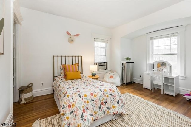 bedroom with radiator, wood finished floors, multiple windows, and baseboards