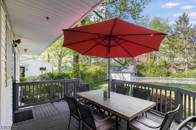 wooden deck featuring outdoor dining space, an outbuilding, a fenced backyard, and a storage unit