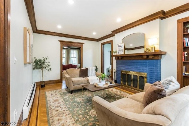 living area featuring baseboard heating, ornamental molding, a fireplace, wood finished floors, and baseboards