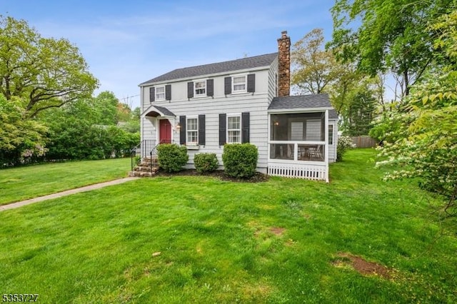 colonial-style house featuring a chimney, a sunroom, a front lawn, and a shingled roof