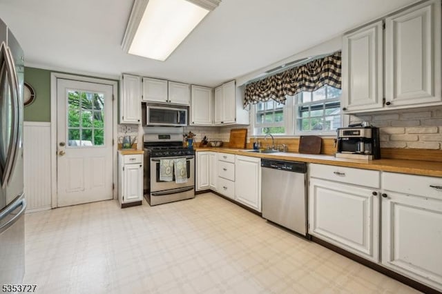 kitchen featuring appliances with stainless steel finishes, a sink, backsplash, white cabinetry, and wainscoting