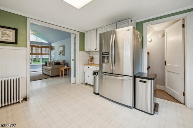 kitchen featuring stainless steel refrigerator with ice dispenser, radiator heating unit, a wainscoted wall, and light flooring