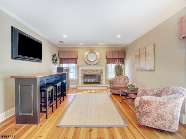 living room featuring baseboards, a stone fireplace, crown molding, and light wood finished floors