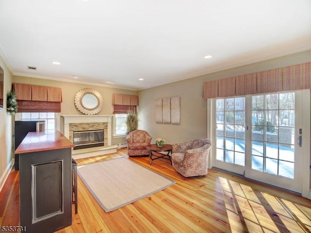 living room with visible vents, recessed lighting, ornamental molding, wood finished floors, and a stone fireplace