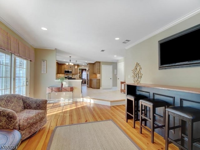 living area with ornamental molding, a chandelier, and light wood-style floors