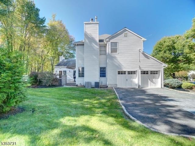 rear view of house with a chimney, driveway, a yard, and an attached garage