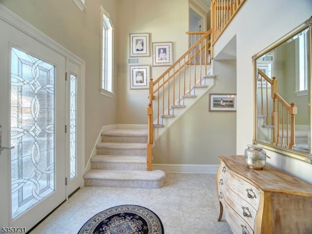 tiled entrance foyer featuring baseboards, visible vents, stairs, and a towering ceiling
