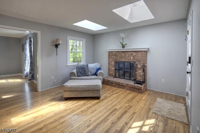 living area with a brick fireplace, wood finished floors, baseboards, and a skylight