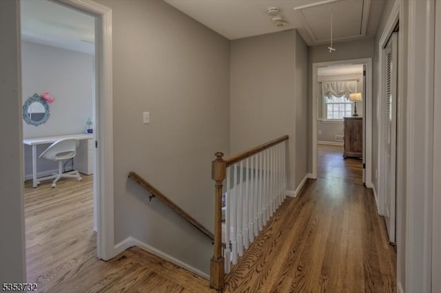 hall with an upstairs landing, attic access, wood finished floors, and baseboards