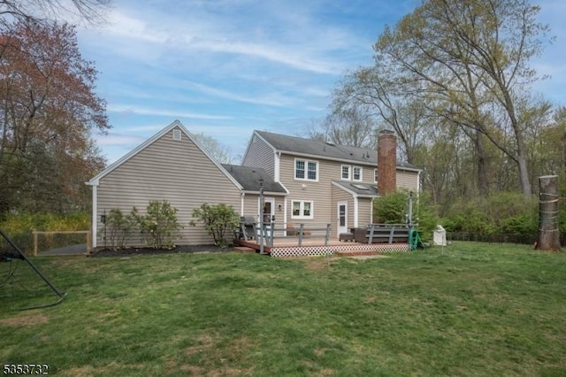 rear view of property with a chimney, a deck, and a lawn
