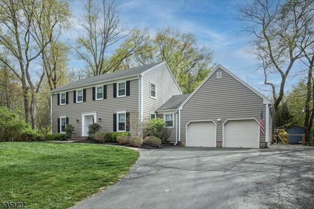 colonial house featuring a garage, a front lawn, and driveway