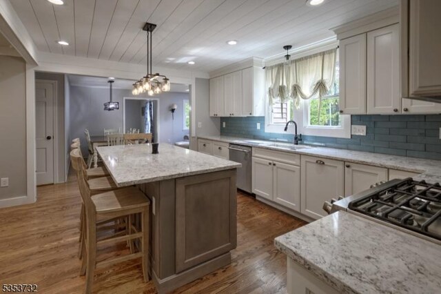 kitchen with a sink, backsplash, a kitchen island, stainless steel dishwasher, and wood finished floors