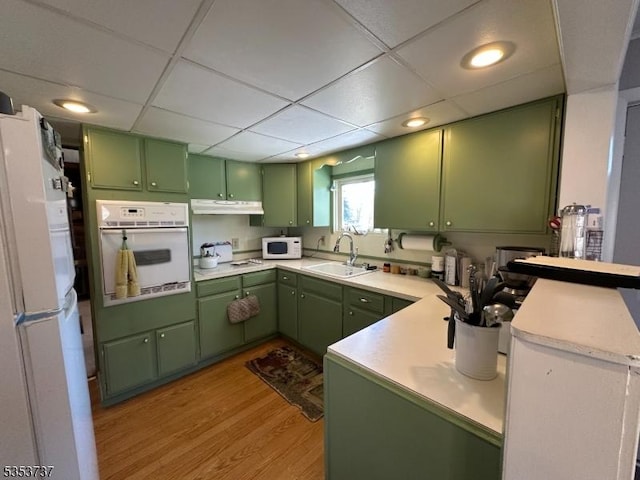 kitchen with green cabinetry, a sink, under cabinet range hood, white appliances, and a peninsula