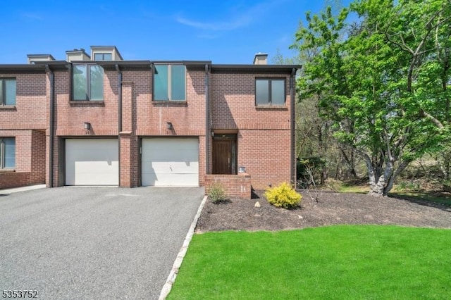 townhome / multi-family property with a chimney, a front yard, a garage, brick siding, and aphalt driveway