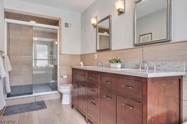 full bathroom with visible vents, tile walls, a sink, toilet, and tiled shower