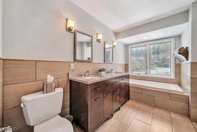 full bathroom with double vanity, toilet, a sink, and a garden tub