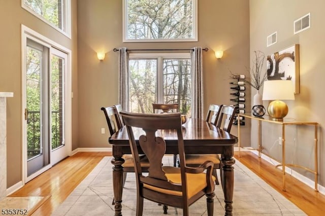 dining room featuring light wood-style floors, visible vents, plenty of natural light, and a towering ceiling