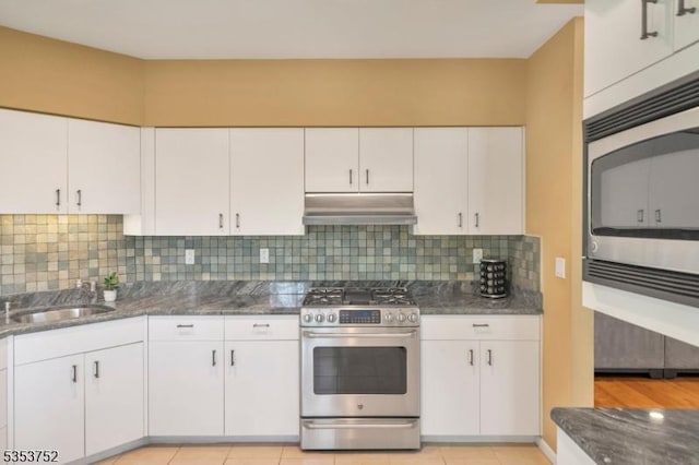 kitchen featuring under cabinet range hood, white cabinets, a sink, dark stone countertops, and appliances with stainless steel finishes
