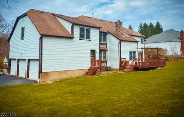 back of property with an attached garage, a wooden deck, a chimney, a lawn, and driveway