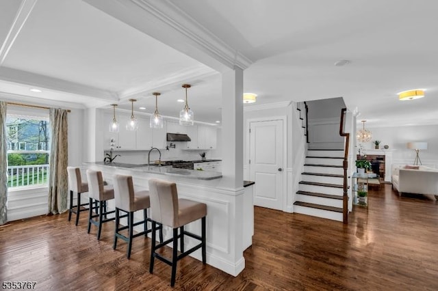 kitchen with white cabinets, a kitchen breakfast bar, a peninsula, under cabinet range hood, and ornamental molding