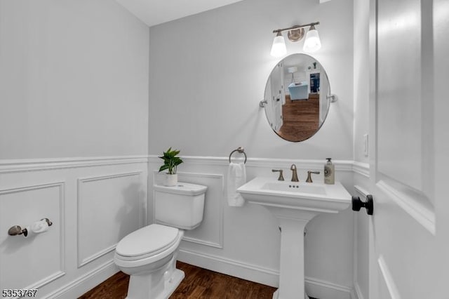half bath featuring wainscoting, wood finished floors, a sink, toilet, and a decorative wall