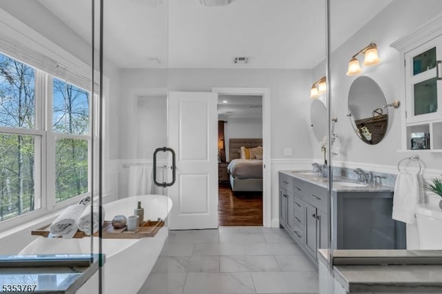 ensuite bathroom featuring ensuite bathroom, plenty of natural light, a wainscoted wall, and visible vents