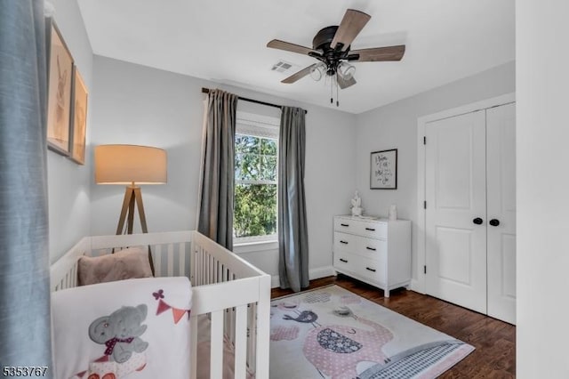 bedroom featuring a ceiling fan, visible vents, wood finished floors, a crib, and a closet