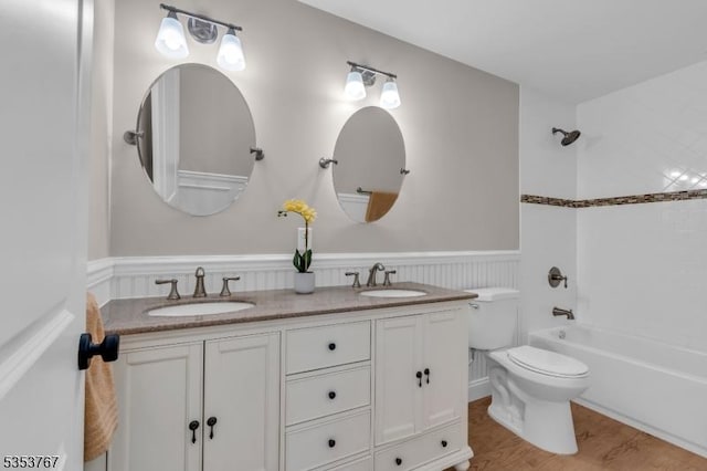 full bath with a sink, a wainscoted wall, toilet, and double vanity