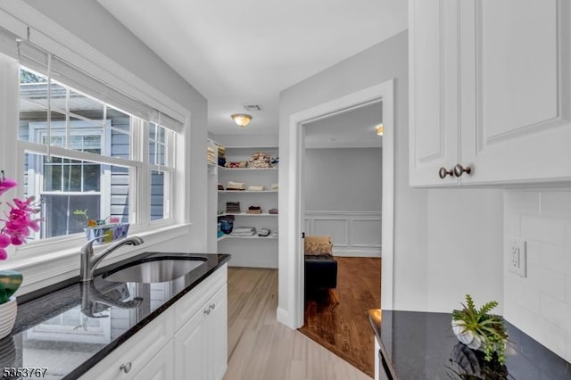 bar with visible vents, wainscoting, a decorative wall, a sink, and light wood finished floors