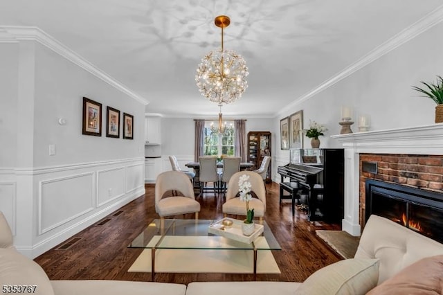 living area featuring crown molding, a fireplace, wood finished floors, and a notable chandelier