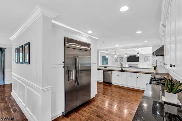 kitchen with white cabinets, a sink, stainless steel appliances, a peninsula, and ornamental molding