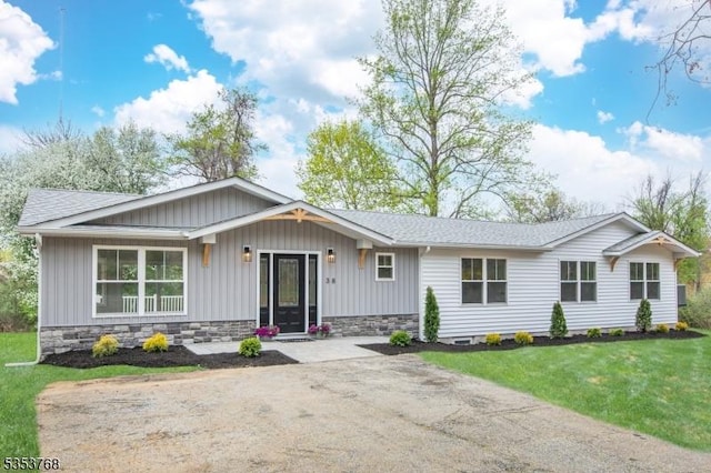 ranch-style house featuring board and batten siding, a front lawn, and roof with shingles